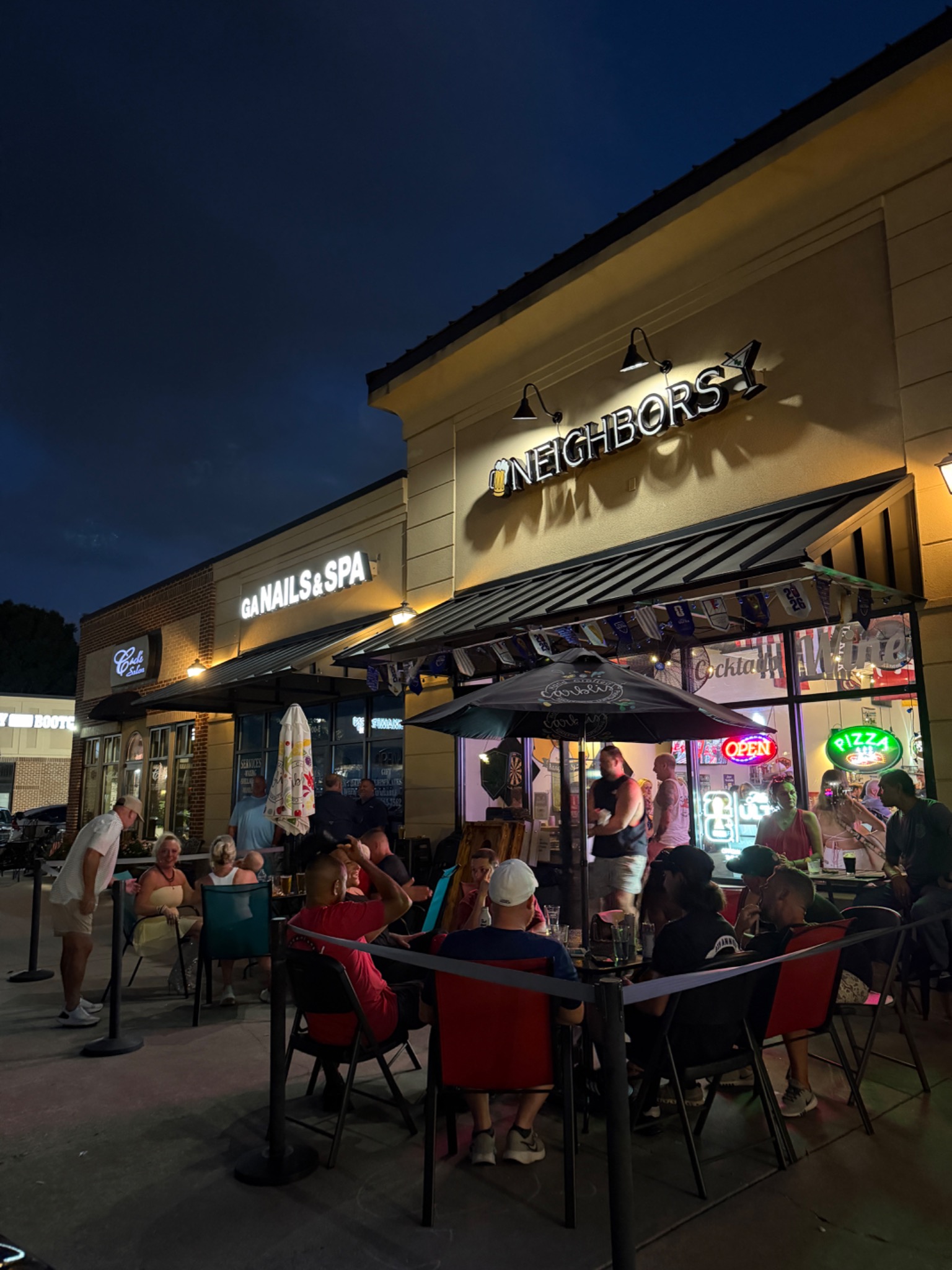 Neighbors Bar's illuminated sign, entrance, and patio at dusk